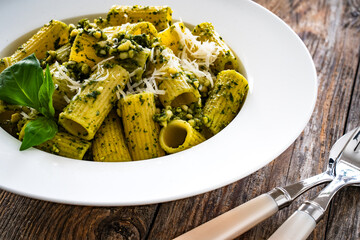 Pasta with basil pesto sauce and parmesan served in white bowl on wooden table
