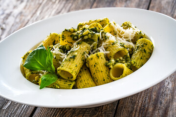 Pasta with basil pesto sauce and parmesan served in white bowl on wooden table
