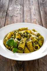 Pasta with basil pesto sauce and parmesan served in white bowl on wooden table
