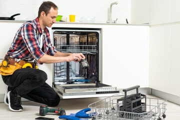 Professional worker repairing the dishwasher in the kitchen