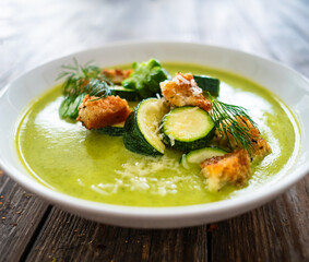 Cream zucchini soup with croutons, Parmesan cheese and fresh dill served in white bowl on wooden table
