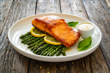 Fried salmon steak with cooked green asparagus and mayonnaise served on wooden table

