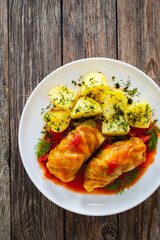Wrapped minced meat in cabbage leaves served in tomato sauce with boiled potatoes on white plate on wooden table - polish dish golabki