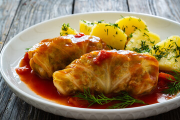 Wrapped minced meat in cabbage leaves served in tomato sauce with boiled potatoes on white plate on wooden table - polish dish golabki