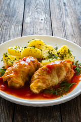 Wrapped minced meat in cabbage leaves served in tomato sauce with boiled potatoes on white plate on wooden table - polish dish golabki