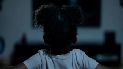 Young child with curly hair watching a suspenseful movie at home on a TV screen at night