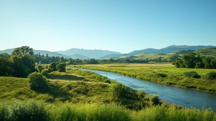 A scenic view from a train window, capturing rolling green hills, distant mountains, and a river running parallel to the tracks, under a clear blue sky.