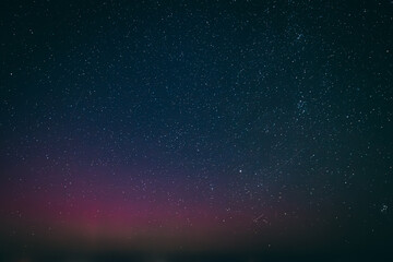 A breathtaking night sky filled with stars, highlighted by a faint aurora borealis in shades of pink and purple, illuminating the horizon above a quiet town. The scene captures the serene beauty 