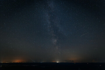 A mesmerizing long-exposure shot captures star trails swirling across the night sky above a brightly lit town. The sky fades from deep blue to purple, creating a stunning cosmic display over the dark