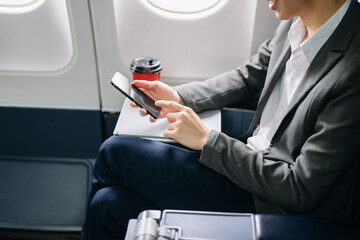 Young Asian executive excels in first class, multitasking with digital tablet, laptop and...