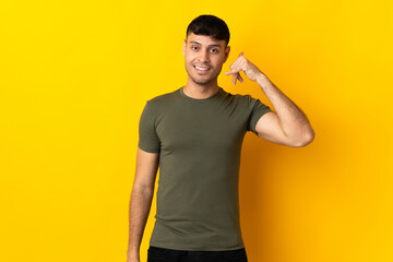 Young Colombian man isolated on yellow background making phone gesture. Call me back sign