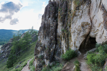 The entrance to a small grotto against the background of dark rocks and forests