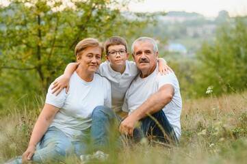 Grandparents with they grandson. They playing on meadow and joying in sunset