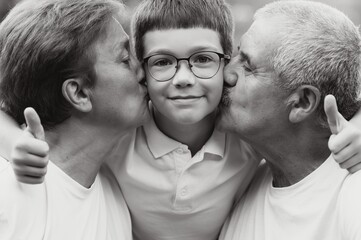 Grandson, grandfather and grandmother sitting on grass having fun outdoors in park at sunset