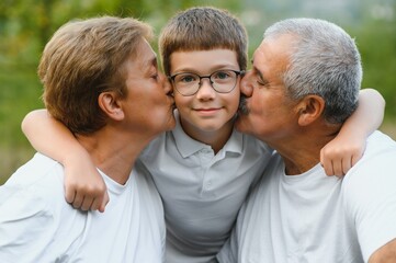 Grandson, grandfather and grandmother sitting on grass having fun outdoors in park at sunset