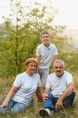 Fototapeta premium Grandparents with they grandson. They playing on meadow and joying in sunset