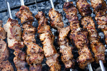 Pork pieces on coals. Pieces of grilled meat on skewers are cooked on hot coals.A barbecue party in nature. Baked pork meat cooked on the grill. Close-up, top view.