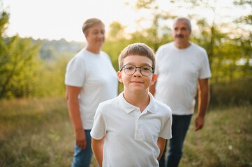 Grandson, grandfather and grandmother sitting on grass having fun outdoors in park at sunset