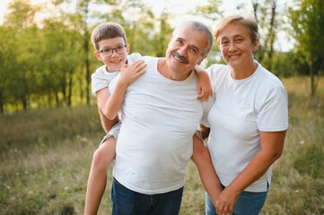 Obraz premium Grandson, grandfather and grandmother sitting on grass having fun outdoors in park at sunset