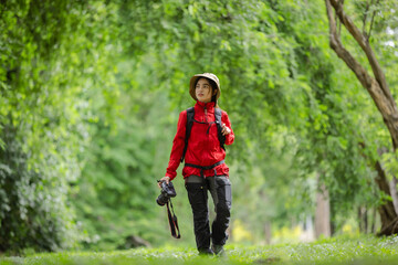 Photographer in a red jacket exploring the lush green park with a camera in hand, capturing...