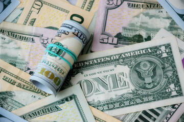 Hundred dollar bills roll lies on big amount of US dollars in different nominations under natural light