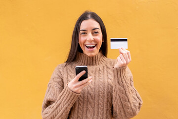 Young brunette woman at outdoors buying with the mobile with a credit card