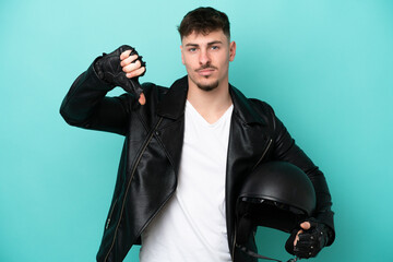 Naklejka premium Young caucasian man with a motorcycle helmet isolated on blue background showing thumb down with negative expression
