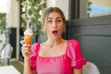 Young blonde woman with a cornet ice cream at outdoors with surprise and shocked facial expression