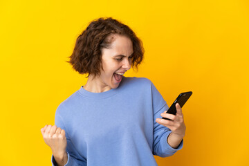 Young English woman isolated on pink background using mobile phone and doing victory gesture