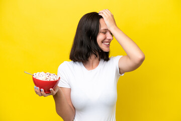 Young caucasian woman holding a bowl of cereals isolated on yellow background has realized...