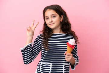 Little caucasian girl holding an ice cream isolated on pink background smiling and showing victory sign