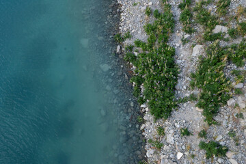 A beautiful and serene view of the turquoise clear water in Lake Tekapo and the small bush of...