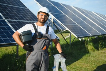 An Indian worker in uniform and with tools works on a solar panel farm