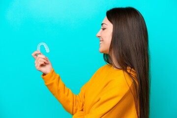 Young caucasian woman holding invisible braces isolated on blue background with happy expression