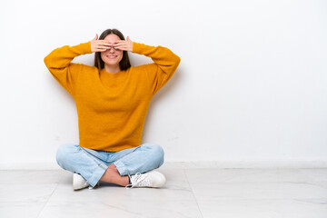 Young girl sitting on the floor isolated on white background covering eyes by hands