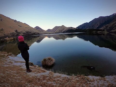 A female standing by the lake looking at the beautiful reflection views of mountains in Moke Lake, Queenstown, New Zealand.  Person standing on the edge of a lake