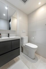 A photo of the modern bathroom in an apartment, white walls with light gray tiles on floor and wall, one black cabinet under sink, toilet is integrated into flooring, 