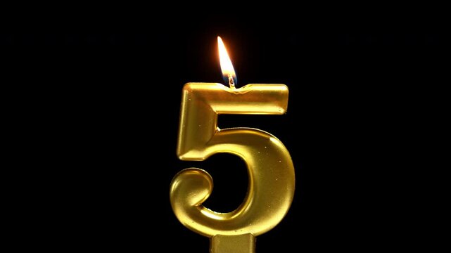 Golden number 5 birthday candle burning against a black background, creating a sleek and elegant celebration scene.