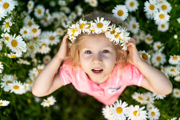 Little happy girl in daisies, close-up portrait on top, child smiling