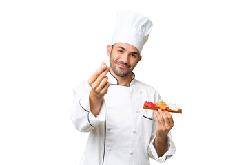 Young caucasian chef holding a sushi over isolated background making money gesture