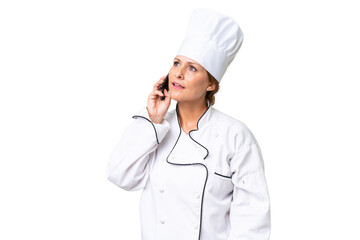 Middle-aged chef woman over isolated background keeping a conversation with the mobile phone