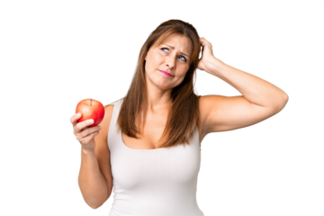 Middle age woman with an apple over isolated background having doubts and with confuse face expression