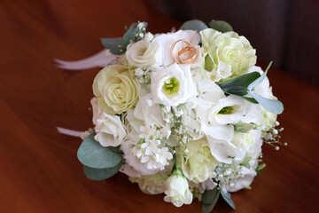 On the table is a wedding bouquet of white roses and two gold wedding rings.