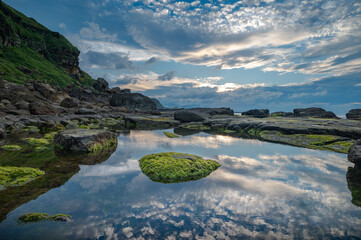 Sunset time in the coastline of Keelung city, ocean reflect the sky and cloud, rocks full of seaweed, in Taiwan.