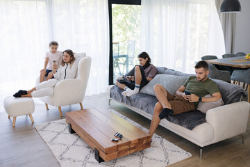 Four person using smartphones at home during sitting on sofa. Family relax in living room. The whole family is glued to their gadgets.