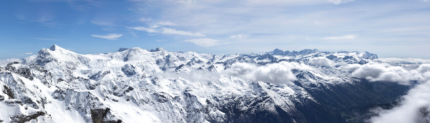 Obraz premium Panoramic view of snow capped Alpine mountains between clouds