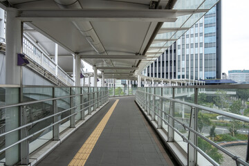 A long, covered pedestrian walkway or footbridge with glass railing connects to a modern building. Modern city infrastructure in Nagoya, Japan