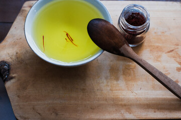 Pile of dried saffron at glasses jar And saffron water mix white cup and wooden spoon in wooden cutting board, herbal tea, healthy drinks.