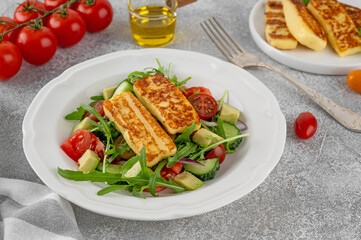 Salad with grilled halloumi cheese, tomatoes, avocado, cucumber and olive oil on a concrete background. Healthy food. Top view