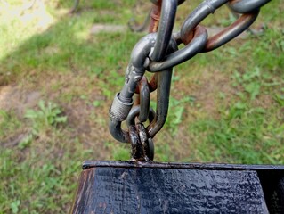Naklejka premium A metal carabiner that is attached to the seat of the swing. Seat attachment on chains. Metal chain.
